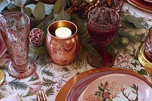 Elegant holiday tablescape featuring deer plates, pink glasses, and glowing can, a Food & Drink Photo by Studio ANNA