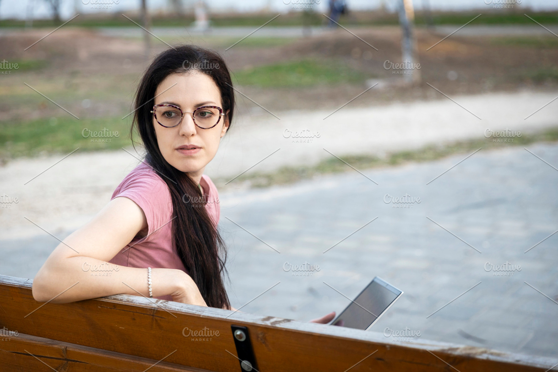 Woman with glasses sitting on a wooden park bench, looking away, a Person Photo by Imaginarium