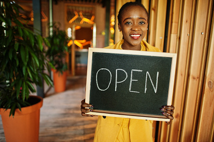 African american woman hold open welcome sign board in modern ca, a Business Photo by AS photostudio