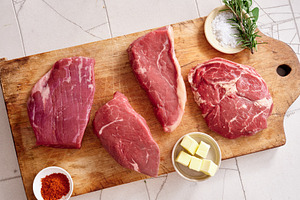 Raw rib-eye, roast beef, flank and rump steak on wooden cutting board with herb, a Food & Drink Photo by Asya Nurullina
