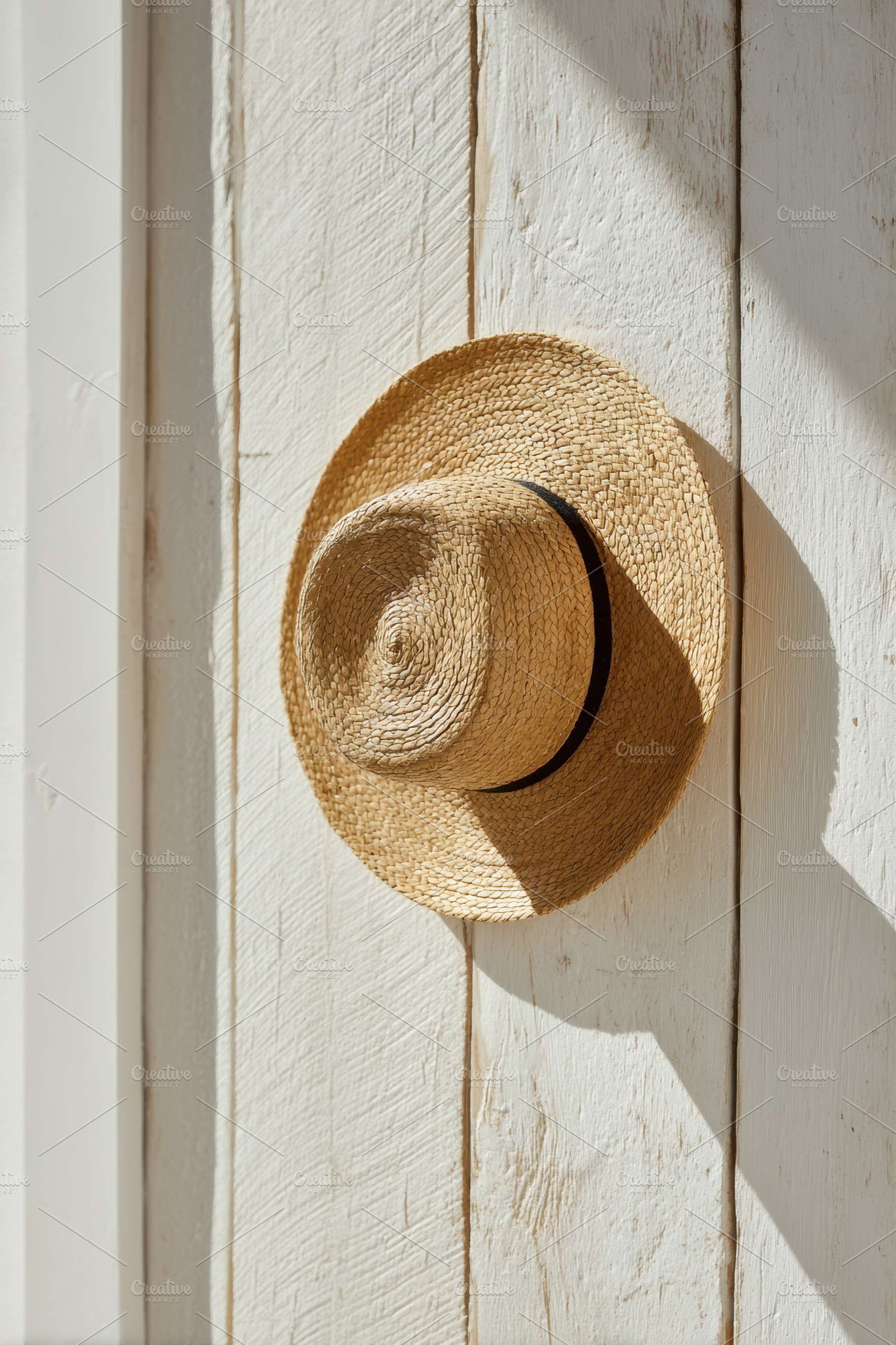 Straw sunhat hanging on wooden wall, a Photo by Virgo Studio