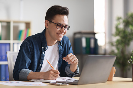Handsome Young Businessman Using Laptop In Office And Taking Notes, a Photo by Prostock-Studio