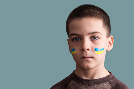 Child against war. Upset Ukrainian boy with bue yellow flag on his face