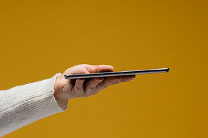 A hand in a white sweater holds a thin modern tablet horizontall, a Technology Photo by ndanko