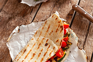 Piadina with grilled zucchini and tomatoes resting on baking paper on wooden ta, a Food & Drink Photo by Antonio Gravante Market