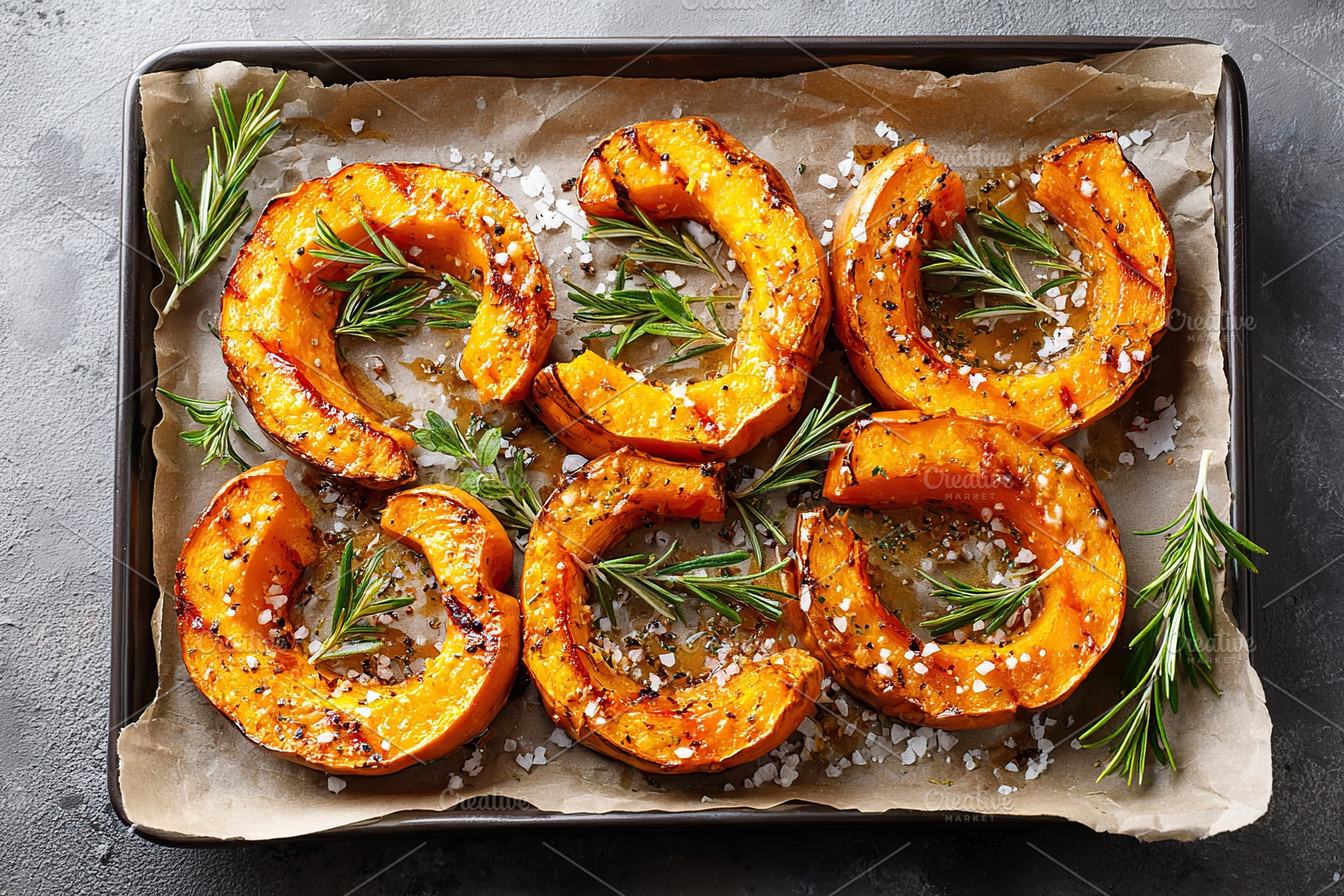 Roasted pumpkin slices garnished with rosemary and coarse salt on a baking tray, a Food & Drink Photo by AlyaAnd