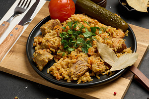 Pilaf with pieces of meat and herbs served on a black plate with, a Food & Drink Photo by ndanko