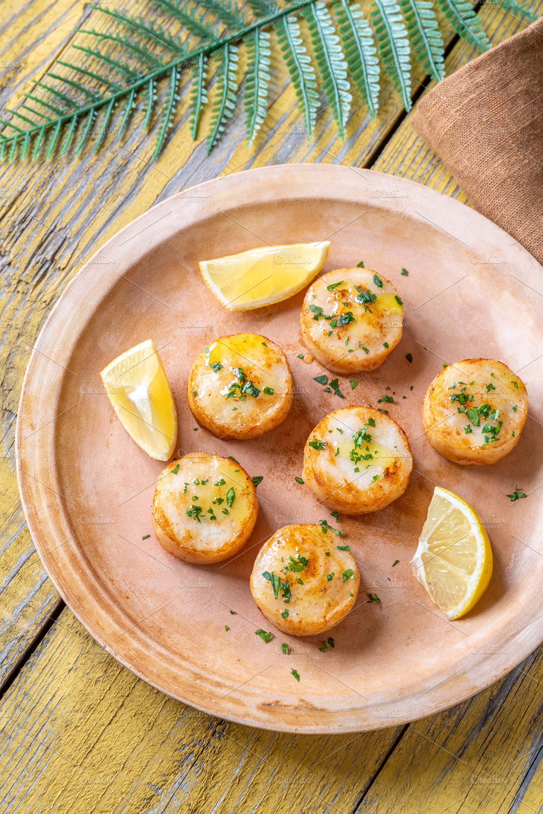 Fried scallops with butter, lemon, parsley on rustic yellow wood, a Food & Drink Photo by Alexander Prokopenko
