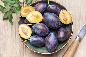 Fresh ripe plums in bowl on wood surface, a Food & Drink Photo by Olena Rudo