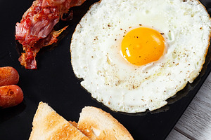 Delicious full English breakfast with fried egg, bacon, sausages and toast on b, a Food & Drink Photo by Antonio Gravante Market