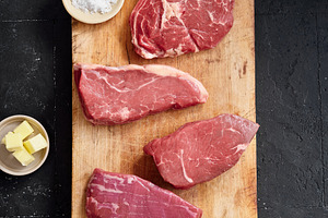 Raw rib-eye, roast beef, flank and rump steak arranged on a wooden cutting boar, a Food & Drink Photo by Asya Nurullina