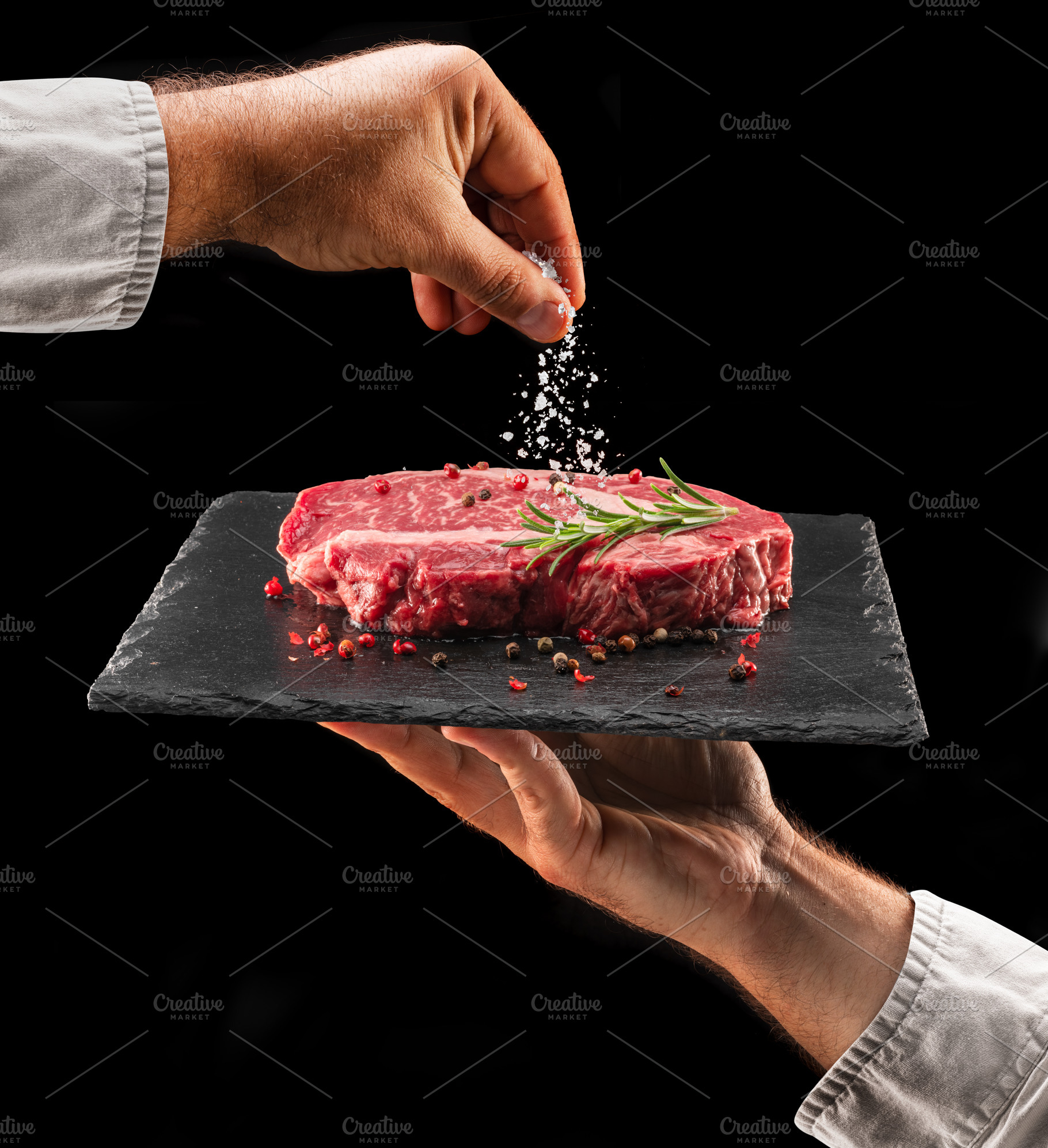 Chef is salting or seasoning raw ribeye steak laying on graphite, a Food & Drink Photo by Volff