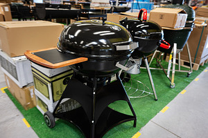 Modern black barbecue grill displayed in a warehouse on artificial green turf, a Photo by AS photostudio