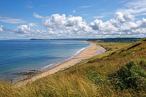 Long sandy beach embracing the ocean, backed by green dunes and, a Photo by Studio ANNA
