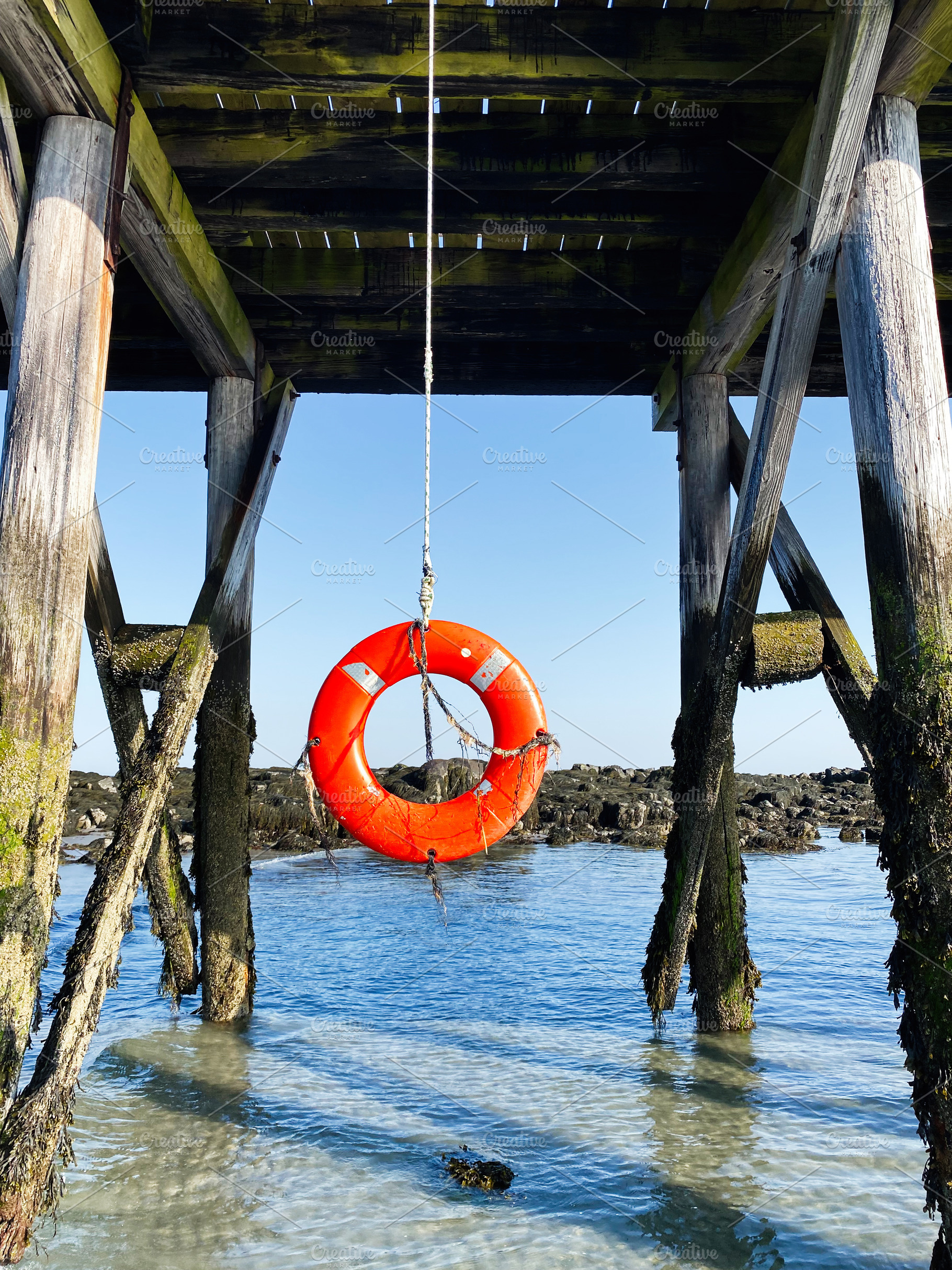 Bright orange lifebuoy hanging under a wooden pier in Portsmouth coastal scene, a Photo by AS photostudio