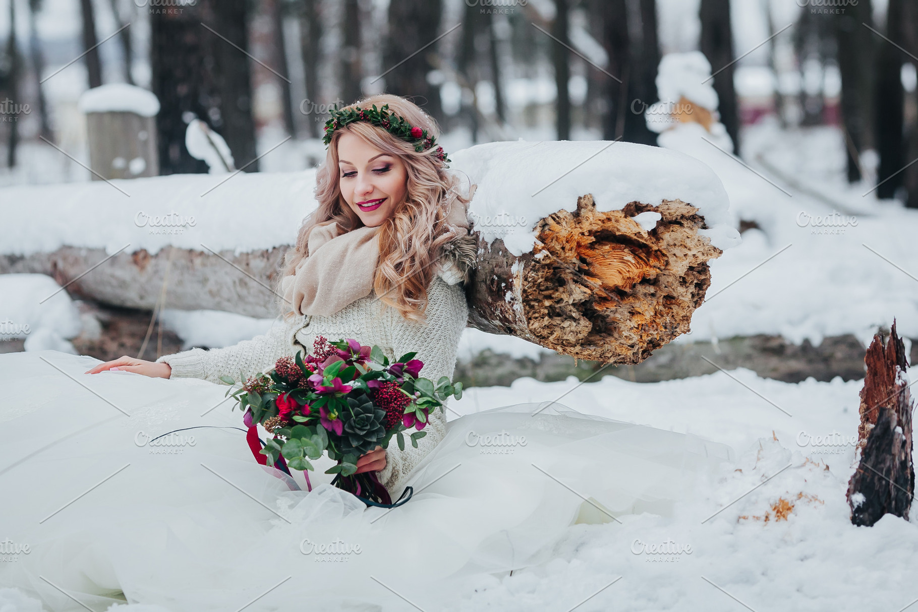 Cute bride sits on the snow near to the wood log and holds a bouquet winter, a Beauty & Fashion Photo by Stahov