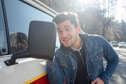 A Young man is pleased to see his handsome looks on the side mirror of a car.