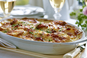 Potato gratin baking in a casserole dish topped with golden cheese and fresh pa, a Photo by Studio ANNA
