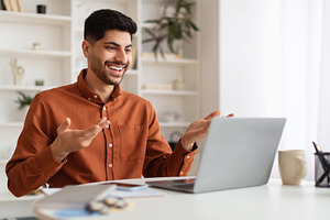 Arab man having video call using laptop and talking, a Photo by Prostock-Studio