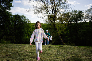 Child running joyfully in a grassy clearing surrounded by lush green trees, a Photo by AS photostudio