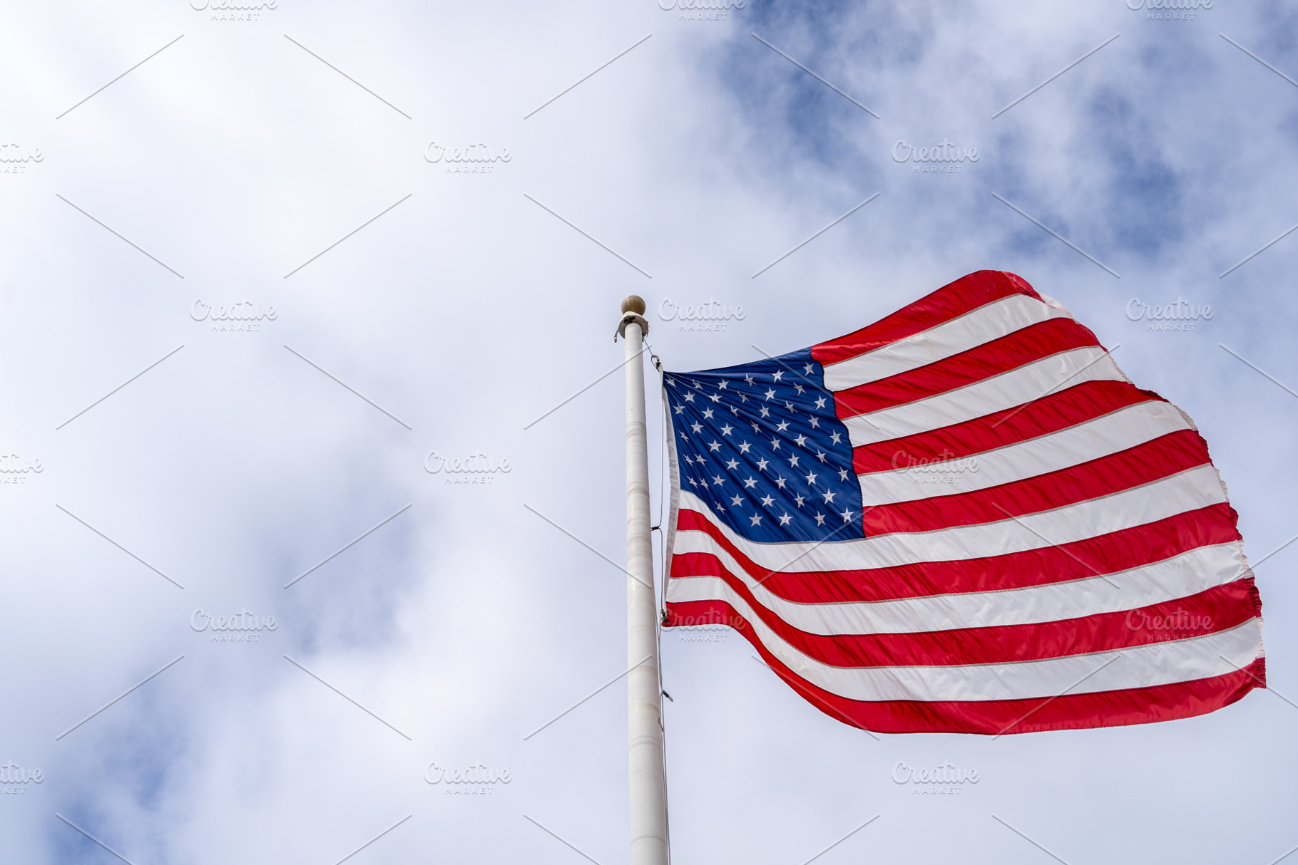 American flag waving on a tall pole against a cloudy sky, a Background Photo by GoodGoods