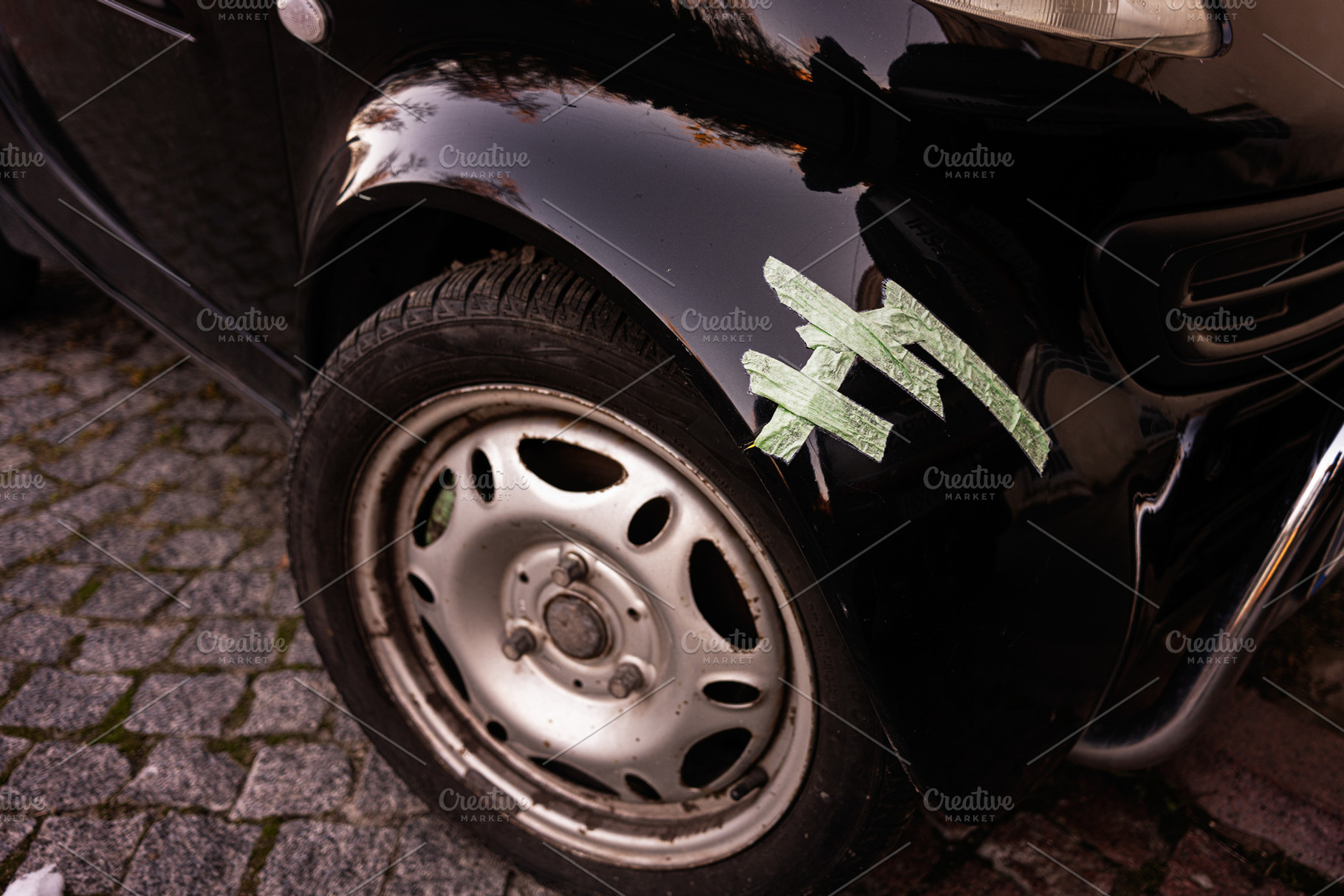 Close-up of a black car with minor body damage and tape repair, a Photo by AS photostudio
