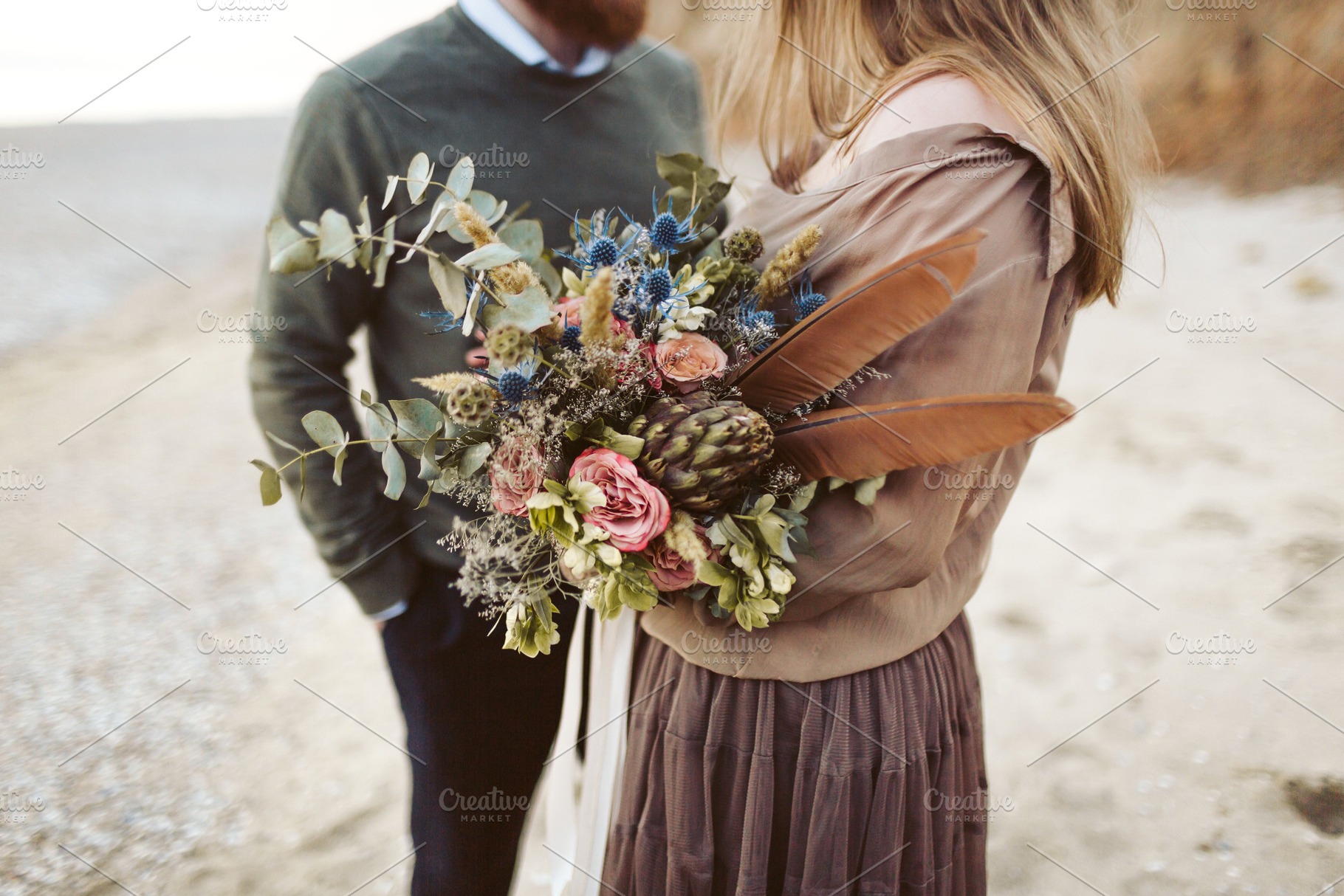 Newlyweds with rustic bouquet in hands stand on seashore. Bride and groom wear in country style clothes and hats., a Person Photo by Stahov