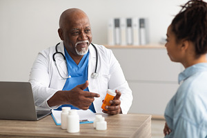 Experienced black doctor showing pills to female patient, a Photo by Prostock-Studio