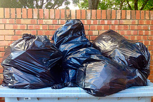Overflowing garbage bin with black plastic bags near brick wall, an Industrial Photo by Antonio Gravante Market