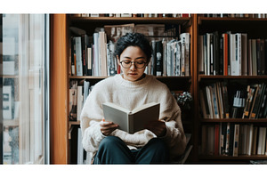 Asian woman reading a book in a, a School & Education Photo by Sergey Kotenev