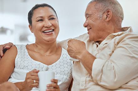 Relax, elderly couple and coffee in a living room with happy, smile and peaceful seniors embracing in their home. Retirement, tea and break with mature man and woman enjoying cozy conversation, a Photo by Peopleimages.com