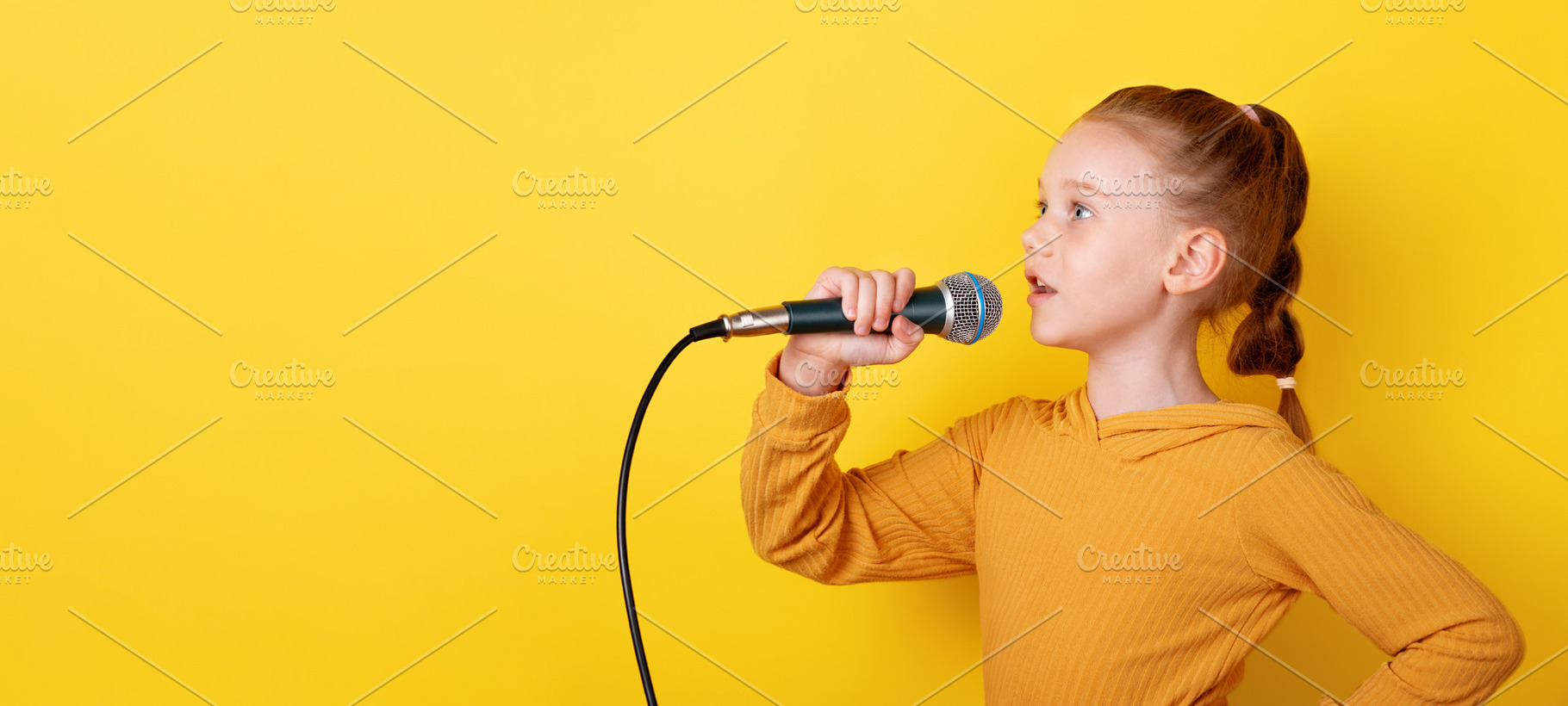 Confident young girl in yellow sweater singing with microphone a, a Person Photo by Ales Munt