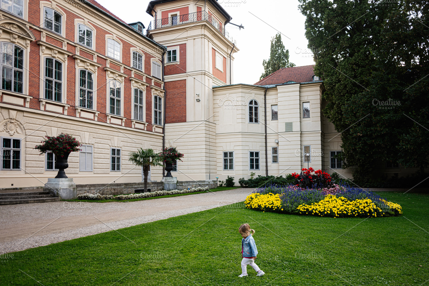 A historic building in Lancut, Poland with a colorful garden and child, a Photo by AS photostudio