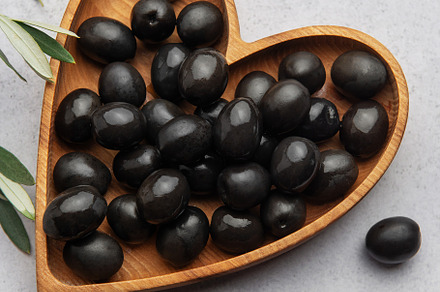Black olives arranged in heart shaped wooden bowl on gray backgr, a Food & Drink Photo by Olena Rudo