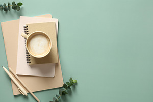 Stack of notebooks, cup of coffee and office supplies on a green background wit
