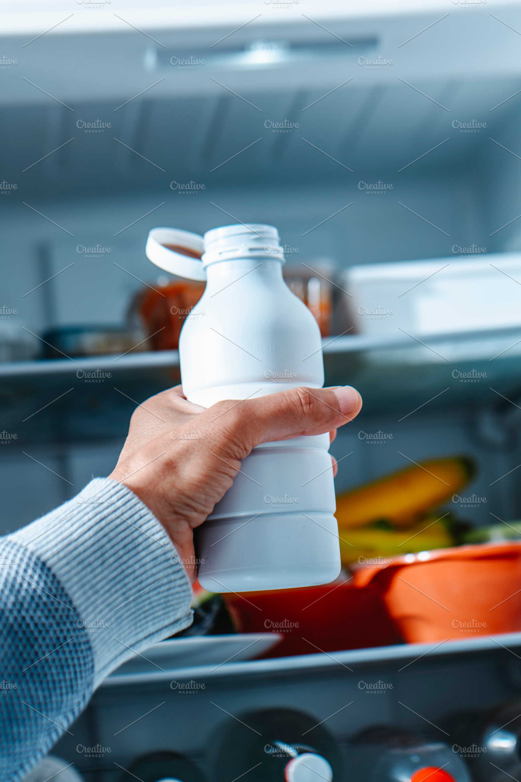 a man reaches for drinkable yogurt in open fridge, a Photo by Nito