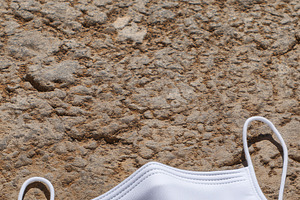 A white face mask mockup lying on a textured stone surface, a Mask Mockup by Textures & Backgrounds