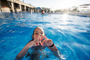 Girl swimming in a pool making a heart gesture on a sunny day, a Photo by AS photostudio