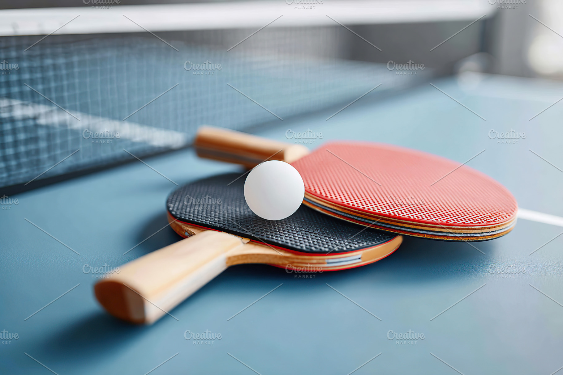 Table tennis paddles and a ball resting on a blue surface with a net in the bac, a Photo by AlyaAnd