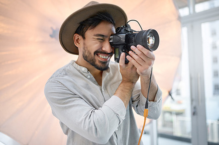 Photography, studio and camera with a man photographer taking a picture backstage during a photoshoot. Creative, light and production with a male using a photographic lens to take a photograph, a Photo by Peopleimages.com