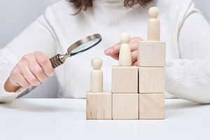 A man with a magnifying glass examines wooden figures on cubes i, a Person Photo by ndanko