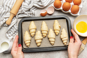 Baker placing tray of raw croissants on table before baking, a Food & Drink Photo by Olena Rudo