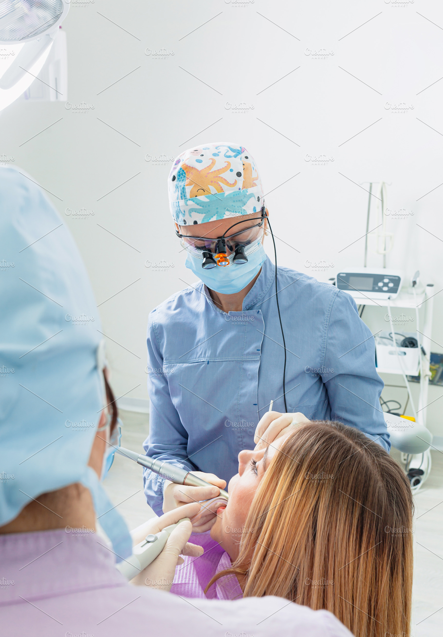 Dentist and assistant performing dental checkup on young woman, a Health & Medical Photo by Antonio Gravante Market