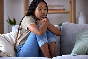Sad, depression and lonely black woman on sofa with mental health issue, problems and stress. Thinking, reflection and depressed girl sitting in living room with mistake, failure and negative emotion, a Photo by Peopleimages.com