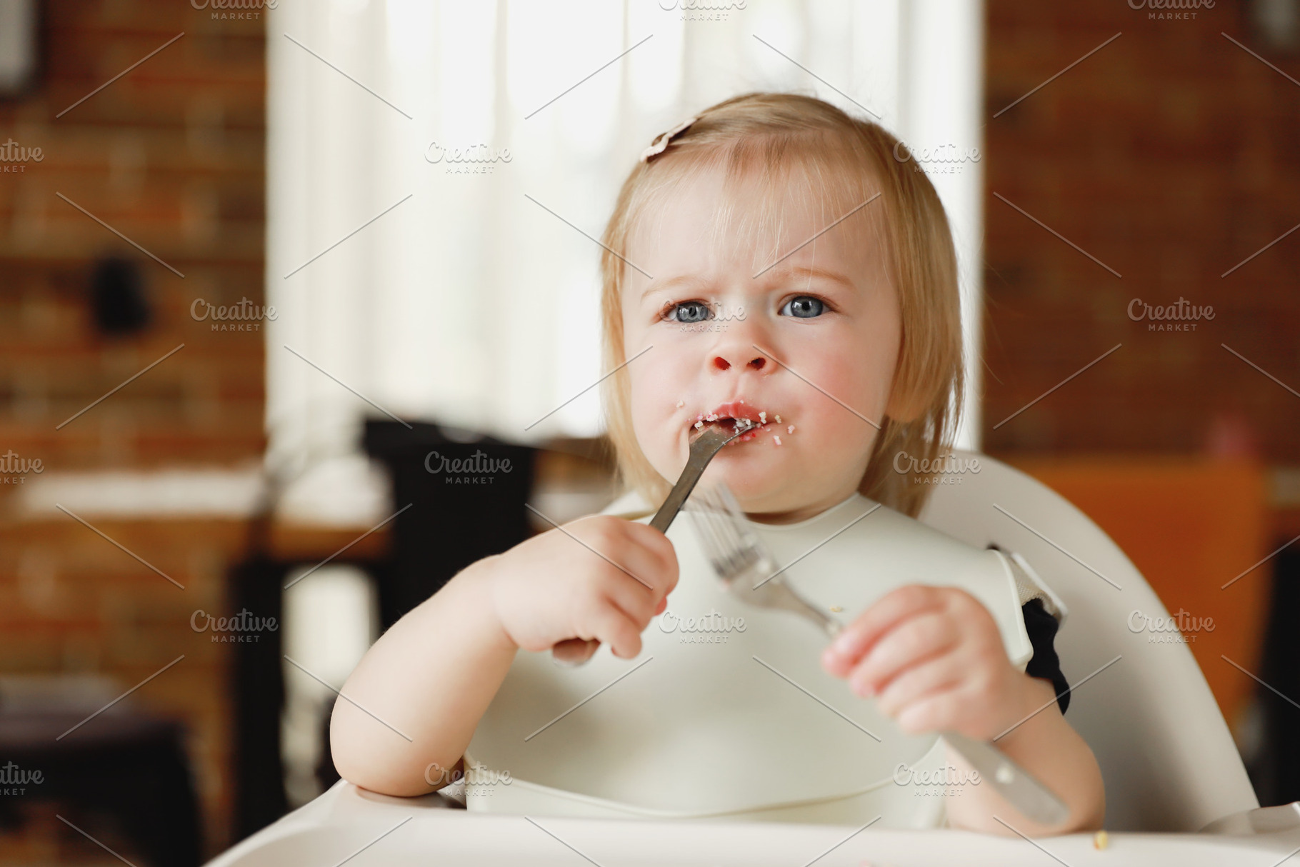Infant girl or toddler sitting on high chair. Eating food by herself using spoo, a Person Photo by Lenor4ik