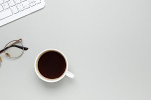 Comfortable workspace setup with coffee cup, keyboard, glasses supporting produ, a Photo by matucha