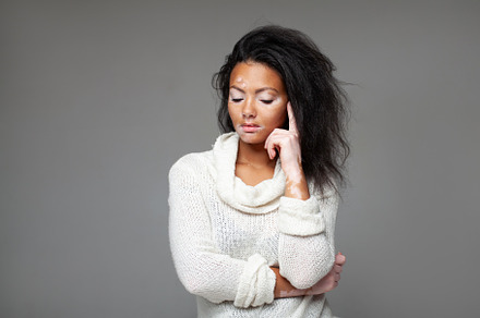 Thoughtful female model with head in hand against gray background