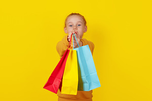 Smiling young girl holding colorful shopping bags on vibrant yel, a Person Photo by Ales Munt