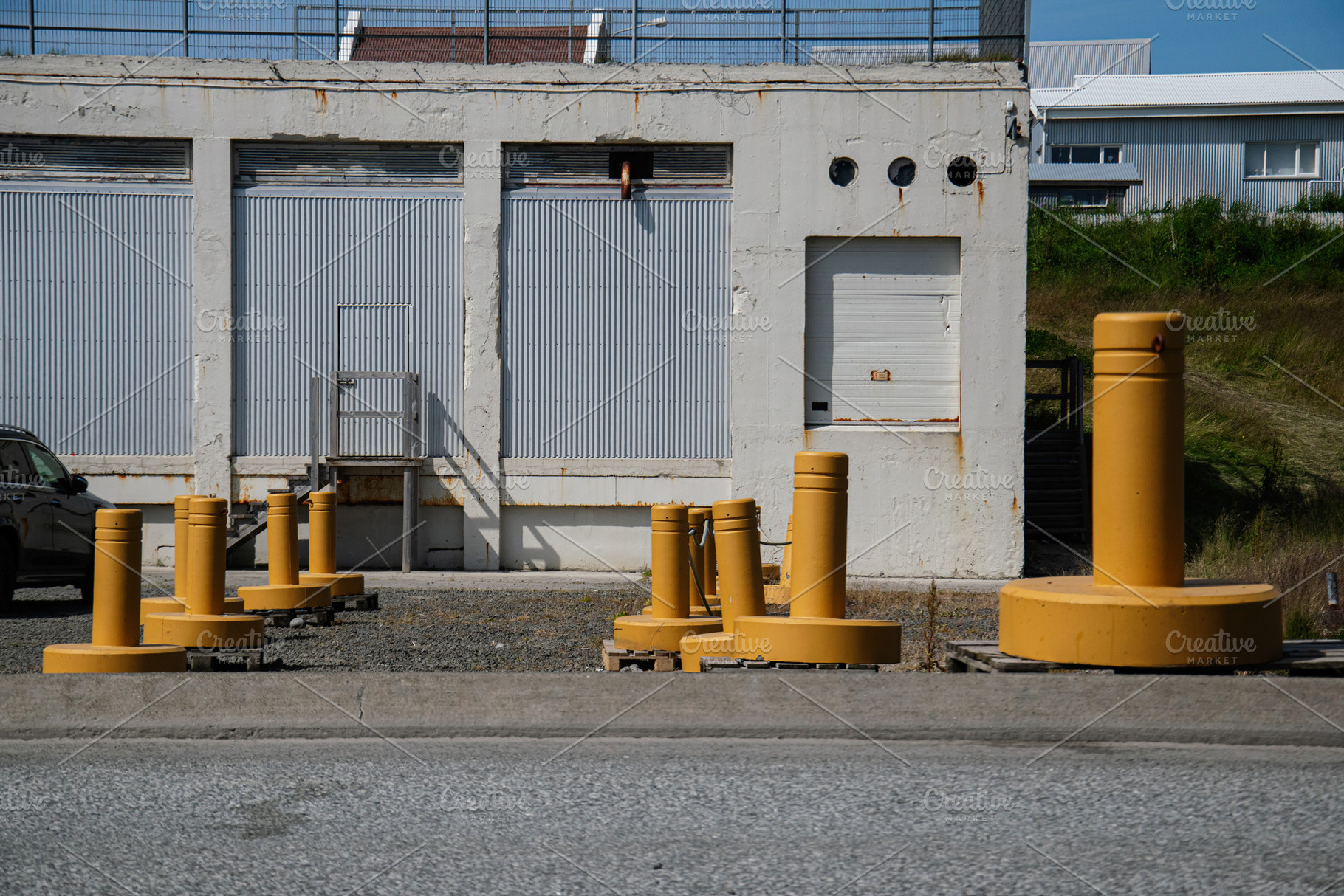 Industrial building exterior with yellow barriers in Akranes, Iceland under sun, a Photo by AS photostudio