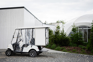 White utility golf cart parked near modern building and landscaped greenery, a Photo by AS photostudio